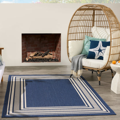 Blue rectangular rug with white border; round wicker egg chair with white cushions and teal starfish pillow beside fireplace.