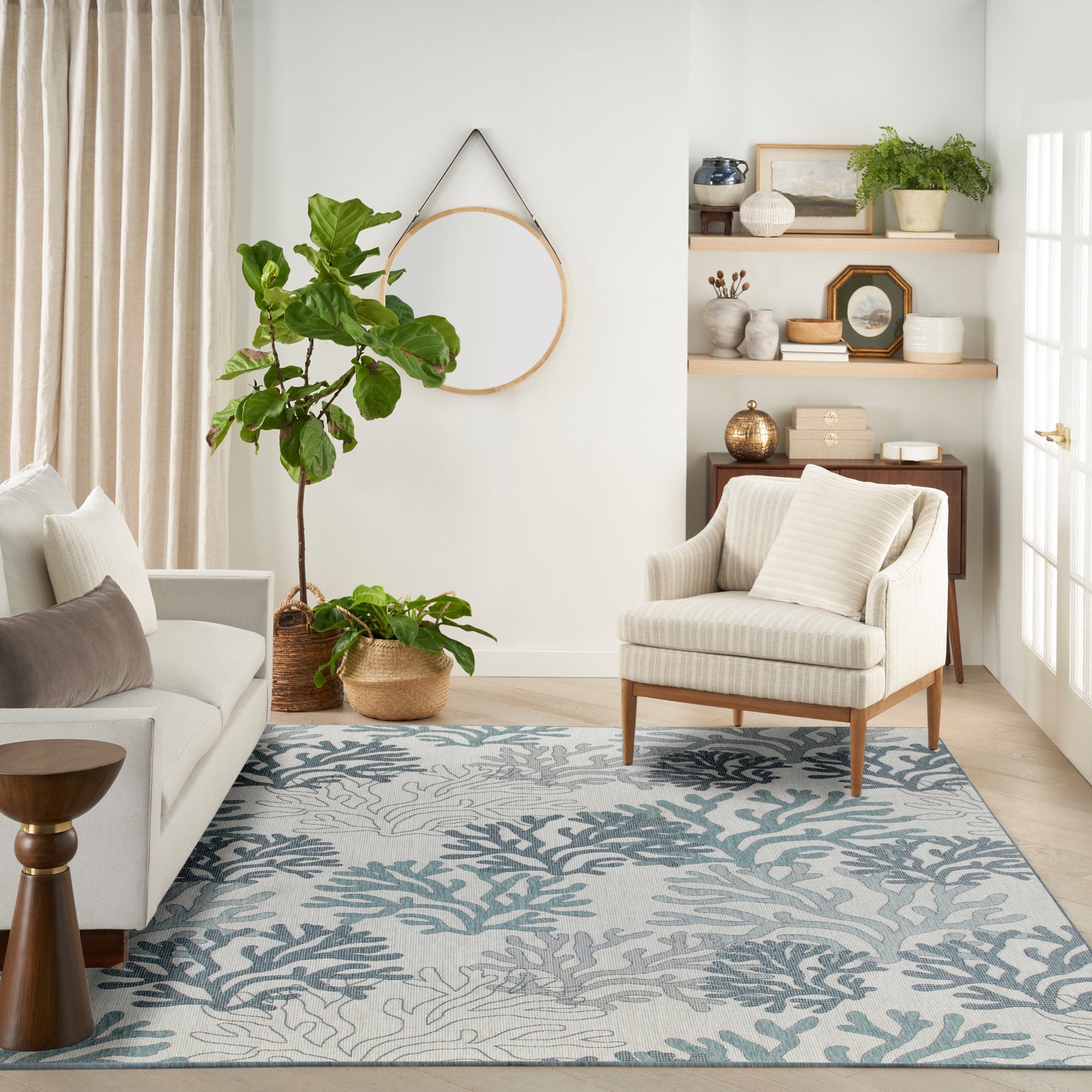 Bright living room with cream sofa, striped armchair, blue-green coral rug, and potted plants on wooden shelves.