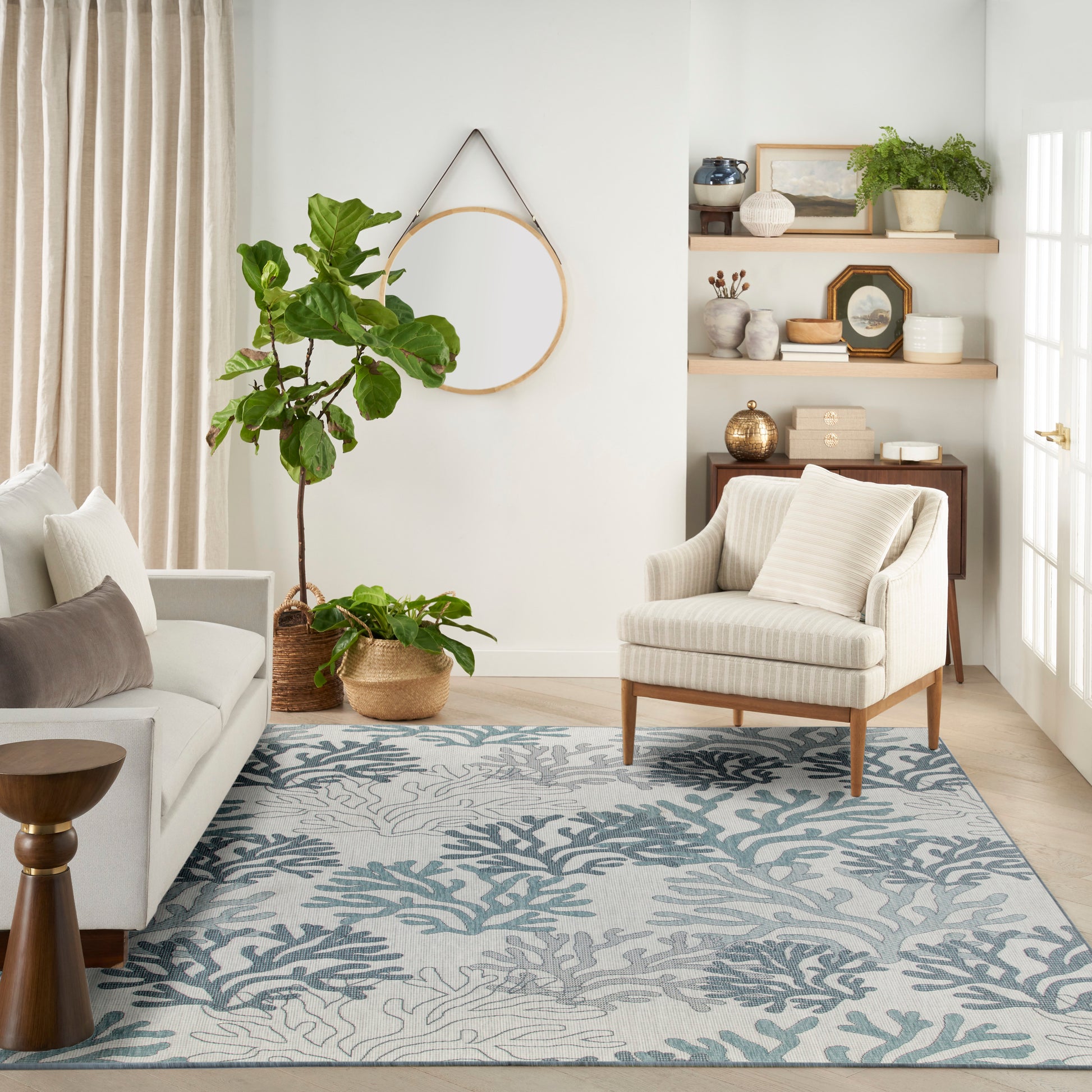 Bright living room with cream sofa, striped armchair, blue-green coral rug, and potted plants on wooden shelves.