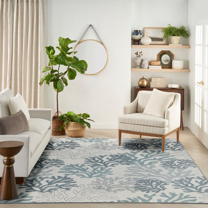 Bright living room with cream sofa, striped armchair, blue-green coral rug, and potted plants on wooden shelves.