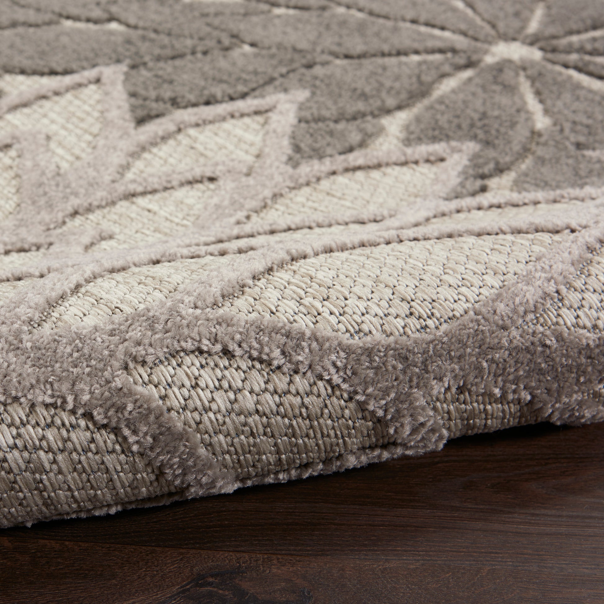 Beige taupe patterned rug with a thick plush pile and leaf motif, edge detail on a dark wood floor.