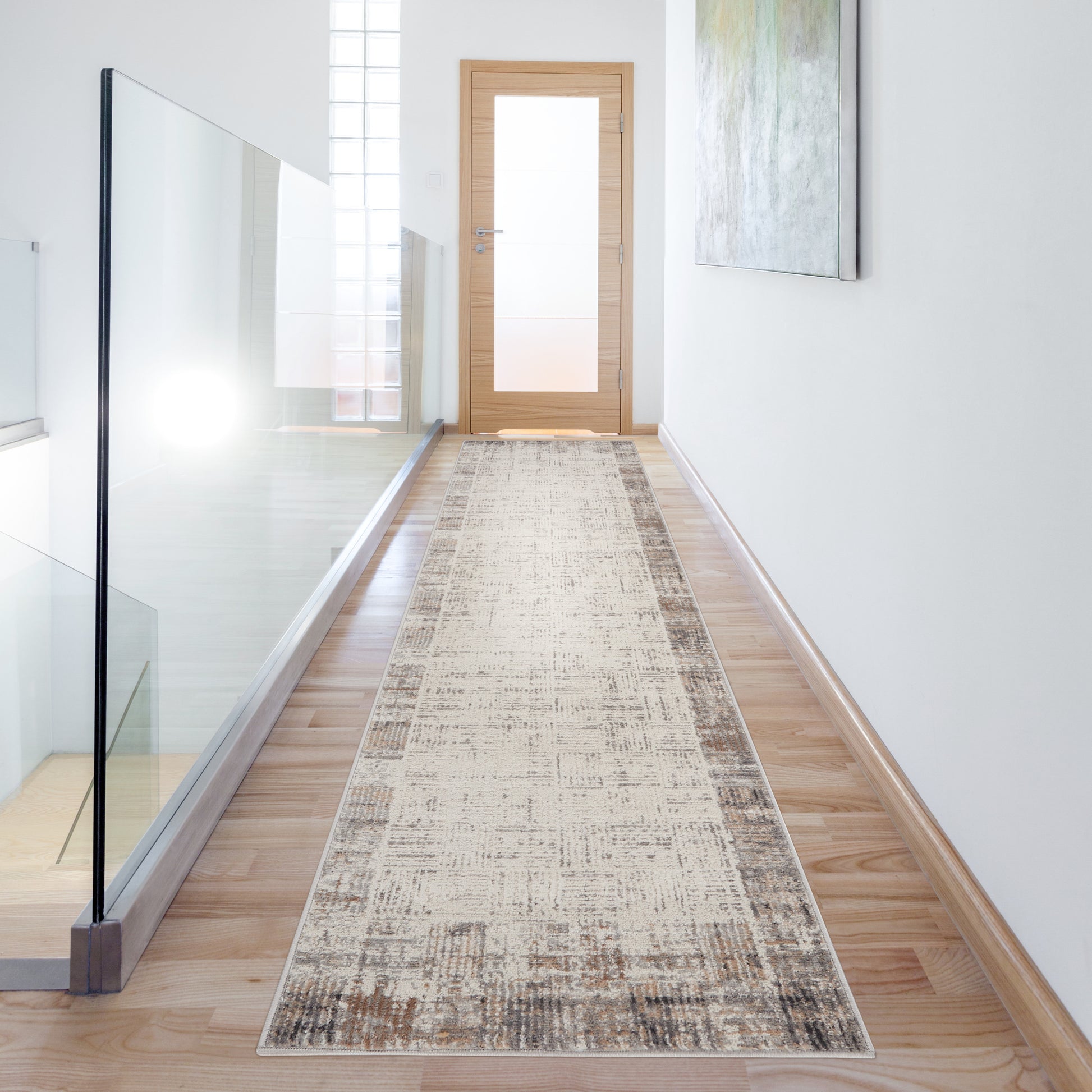 Long beige distressed rug runner along a wood-floor hallway with glass railing and a wooden door at the end.
