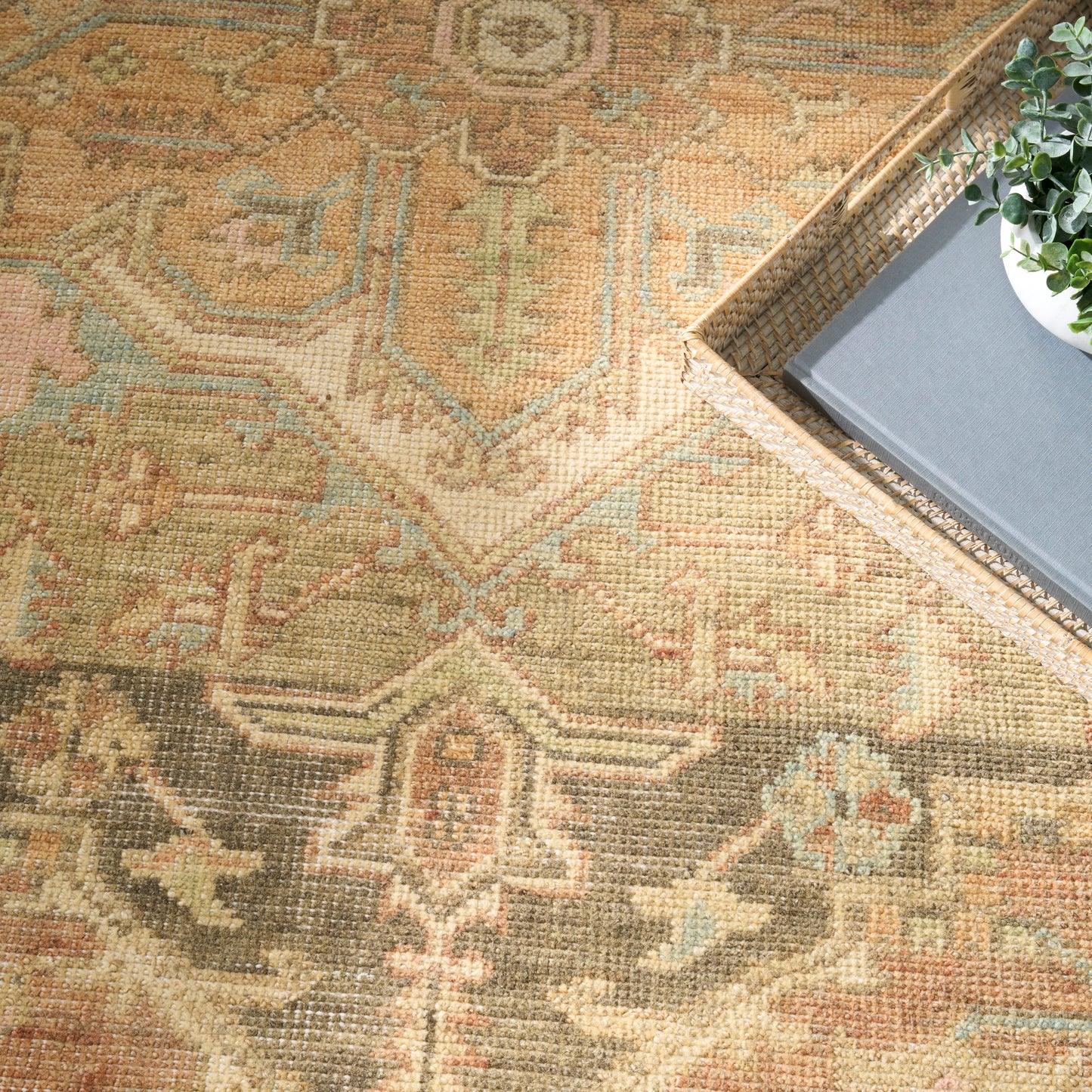 Vintage-inspired Persian-style rug in warm gold, tan, sage and blue; woven texture; tray with plant and book nearby.