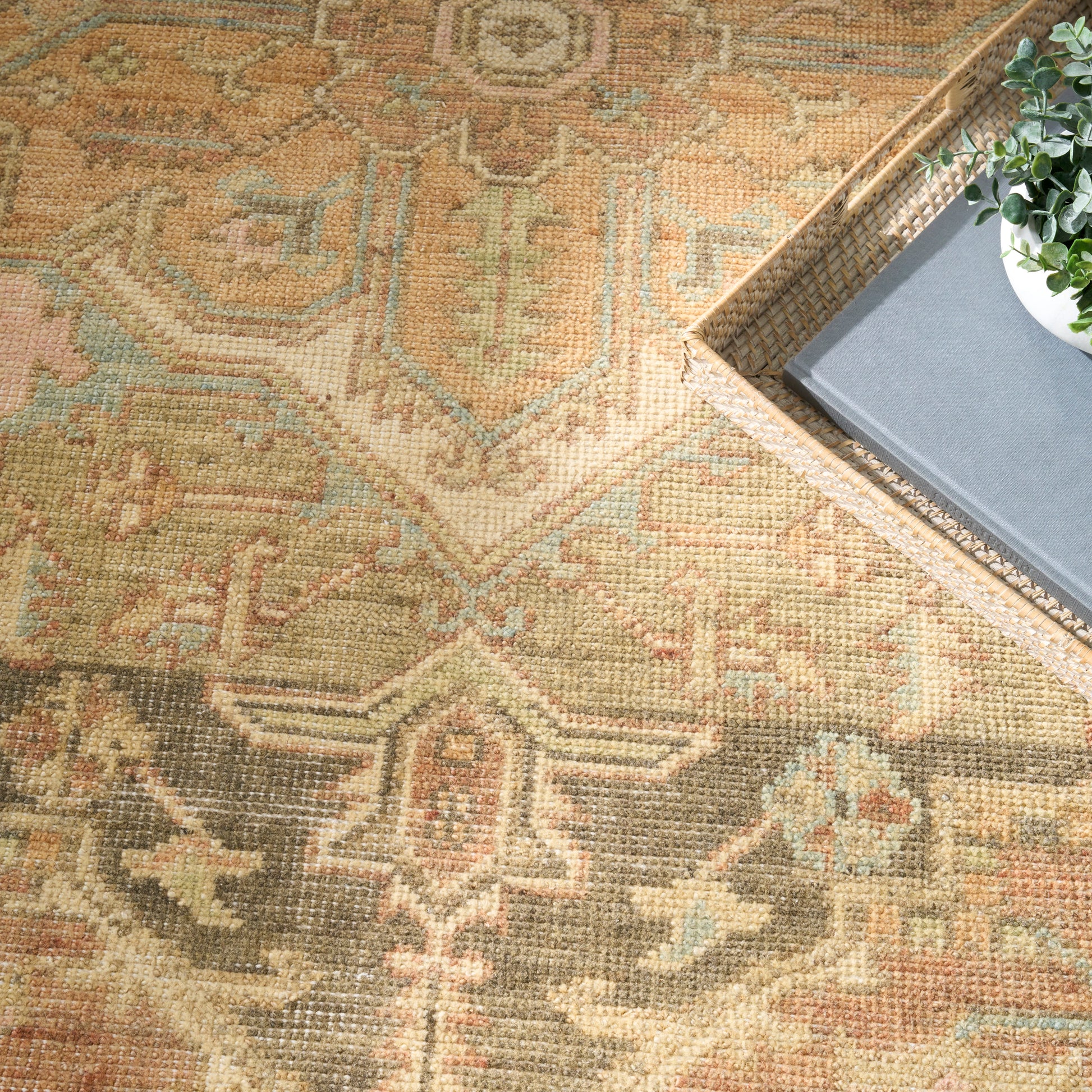 Vintage-inspired Persian-style rug in warm gold, tan, sage and blue; woven texture; tray with plant and book nearby.