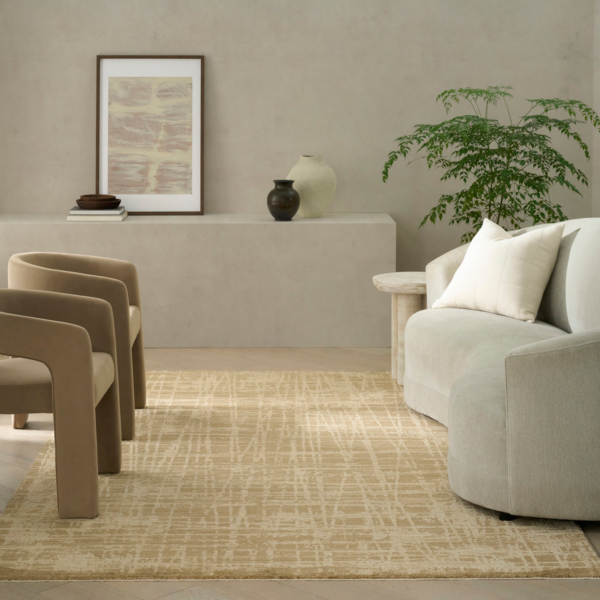 Neutral living room featuring beige curved chairs, light sofa, patterned beige rug, and a console with framed art and pots.