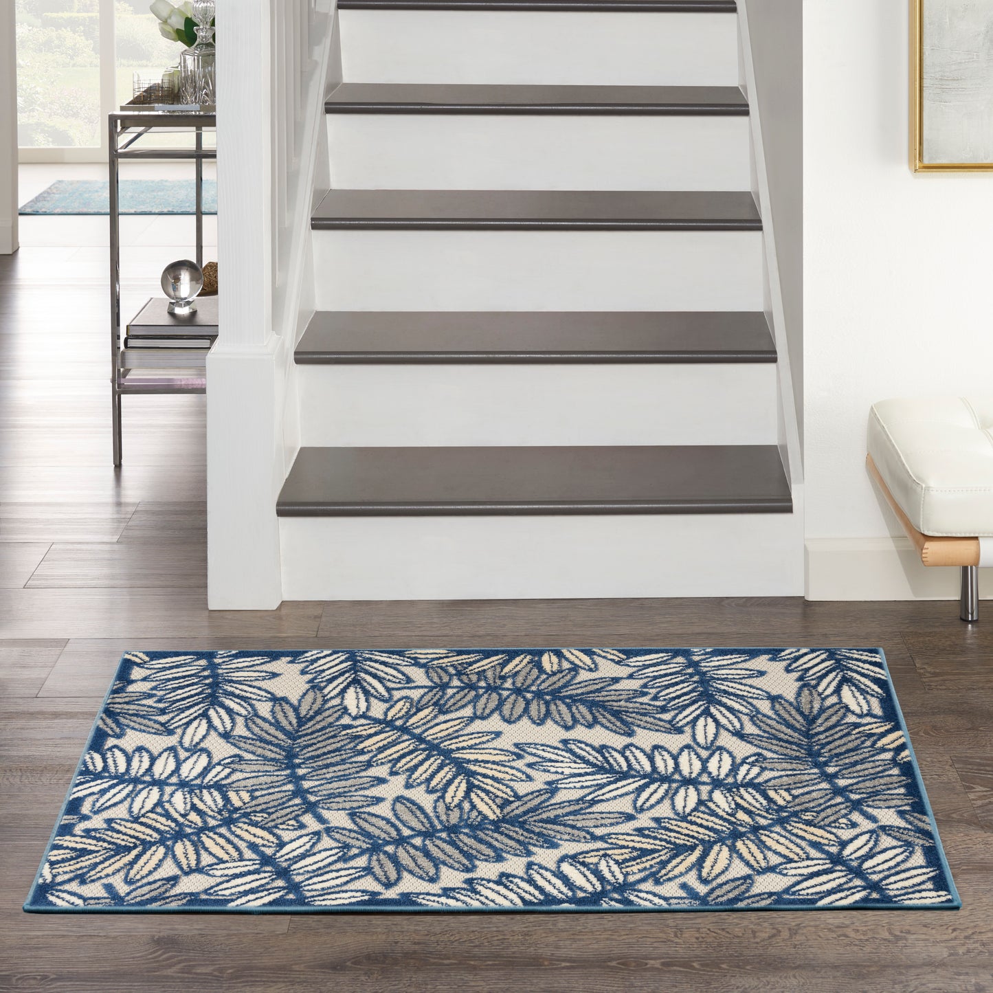 Rectangular blue and white woven rug with a botanical leaf pattern and border, on dark wood floor beside a staircase.