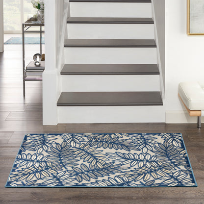 Rectangular blue and white woven rug with a botanical leaf pattern and border, on dark wood floor beside a staircase.