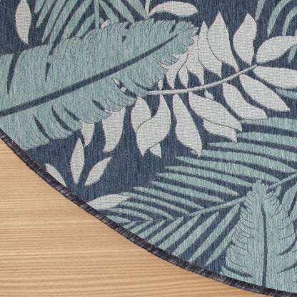 Outdoor round woven rug with teal tropical leaf pattern on navy background; dark bound edge.