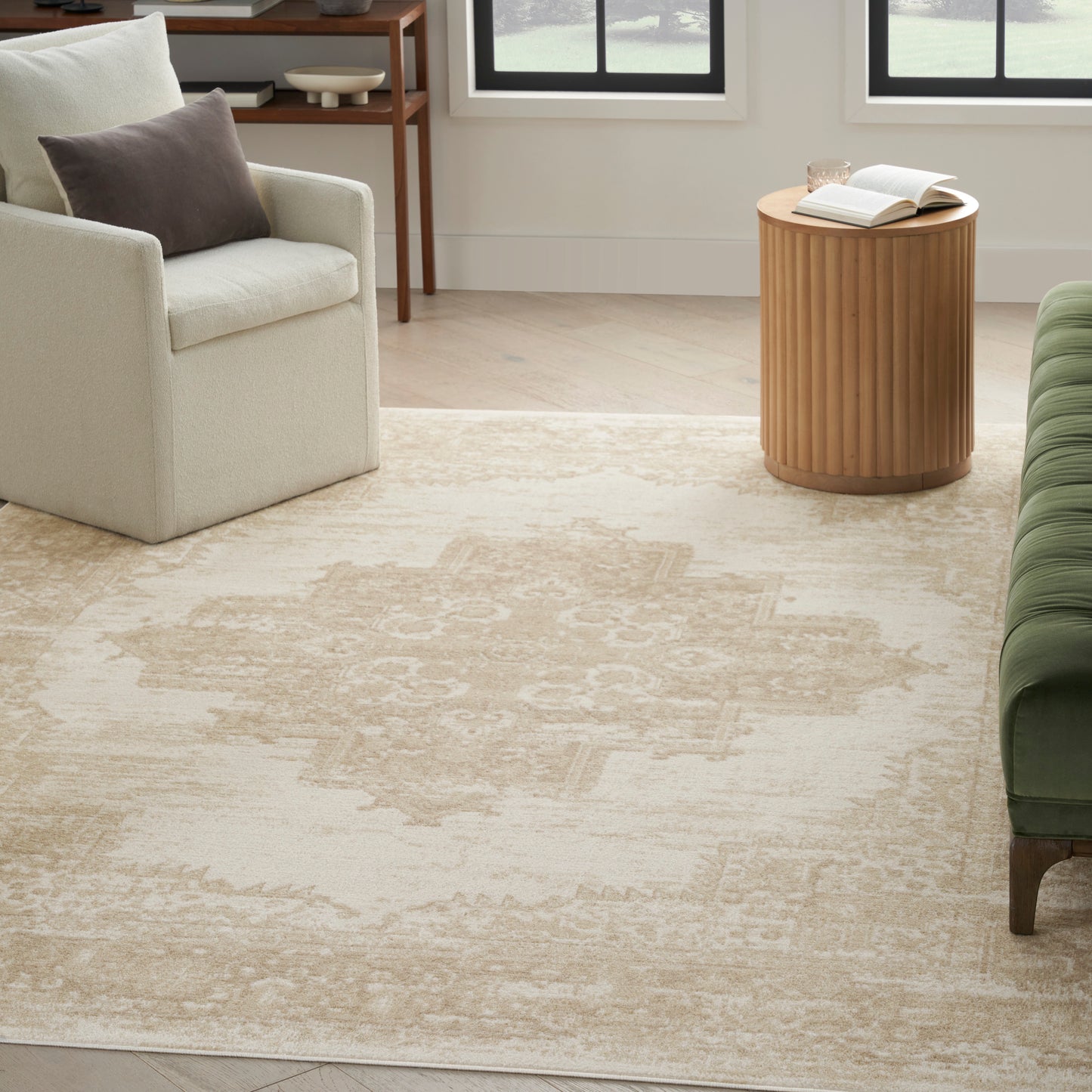 Beige patterned area rug in a modern living room with cream armchair, round slatted wood side table & green sofa.