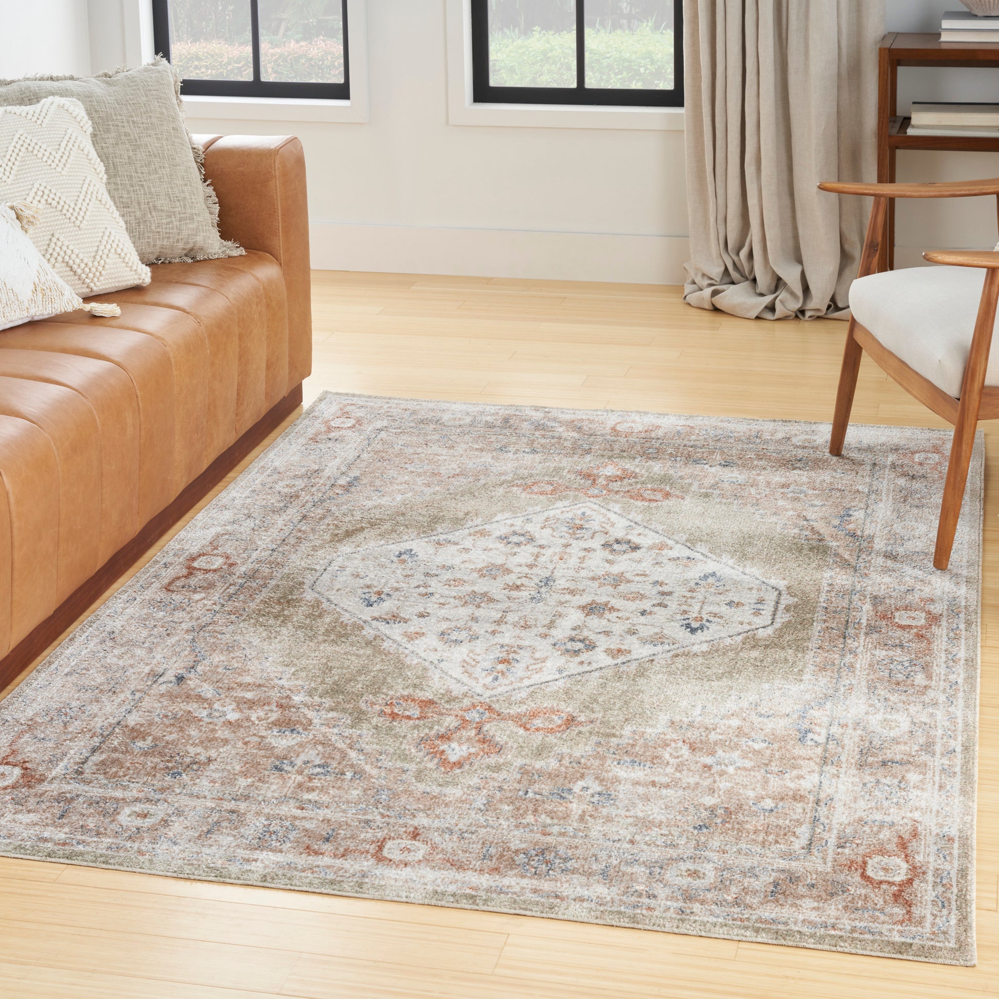 Vintage-style beige area rug with faded geometric medallion pattern on light wood floor beside a tan sofa and wooden chair.