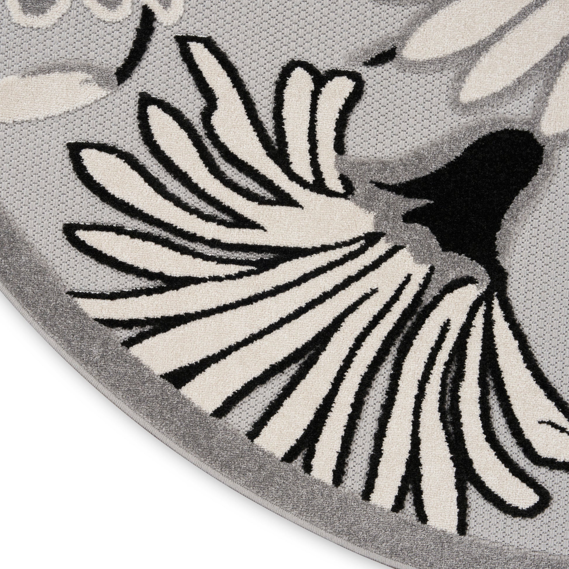 Round grey rug with cream and black floral petal motif and soft woven texture.