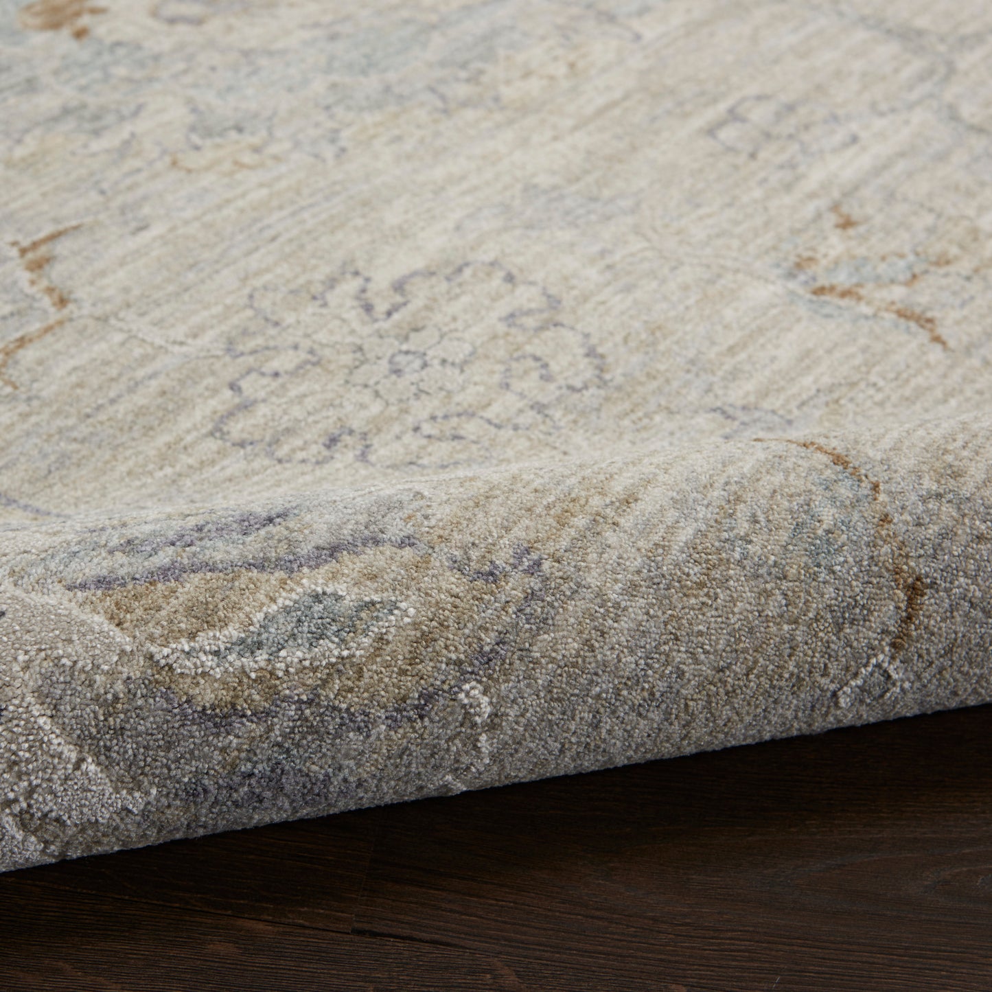 Beige & gray patterned rug with a subtle floral medallion, thick pile, folded edge on dark hardwood floor.