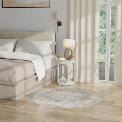 Neutral bedroom with white bedding, light wood floor, round blue-gray rug, white circular side table and lamp.