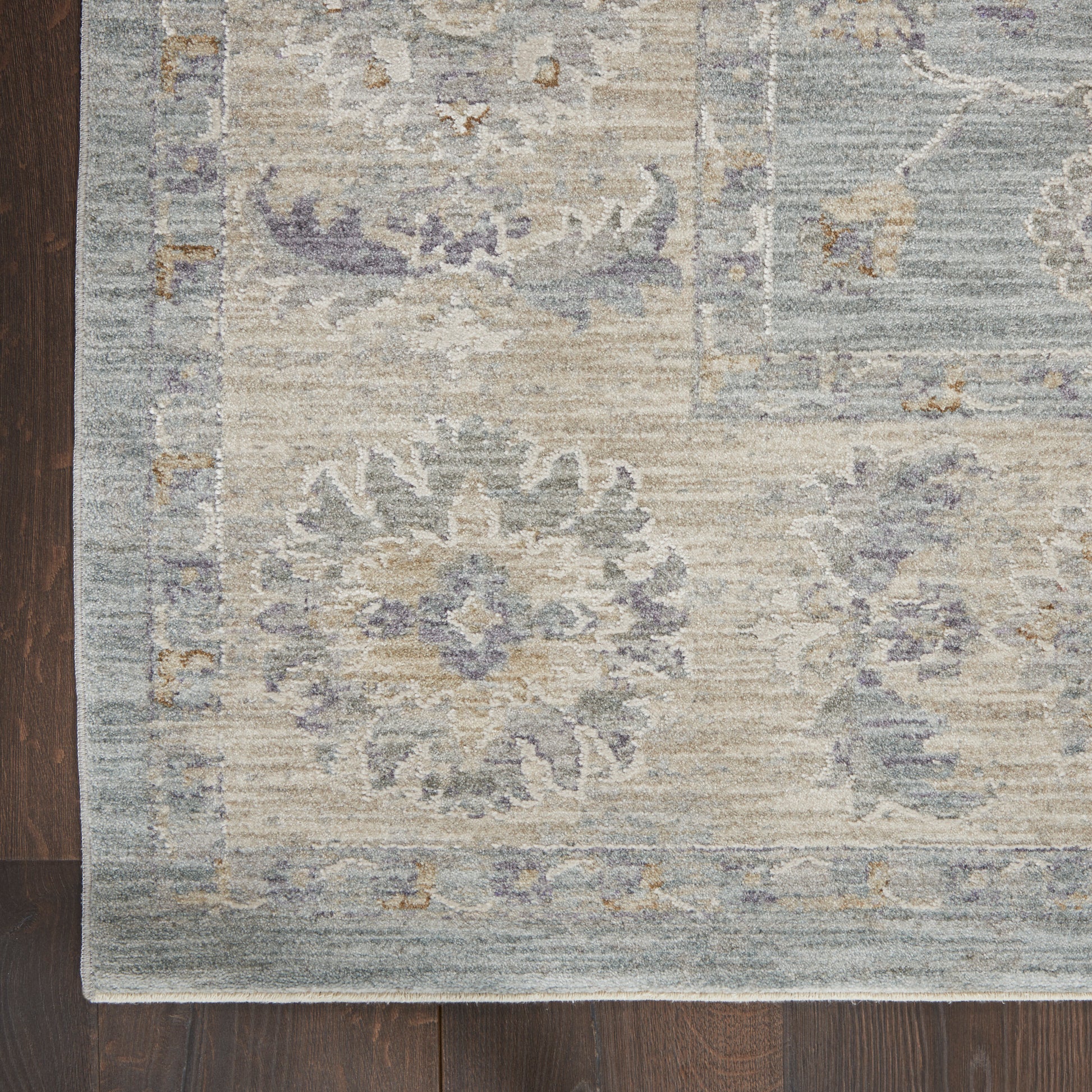Muted blue & ivory distressed oriental rug with floral medallions & a geometric border on a dark wood floor.