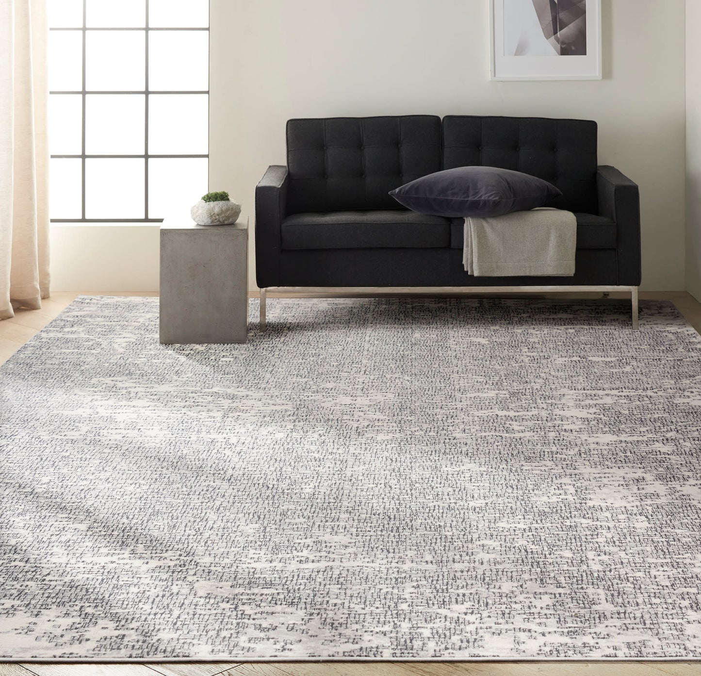 Charcoal tufted sofa on a gray patterned rug in a modern living room with a concrete side table, potted plant & beige curtains