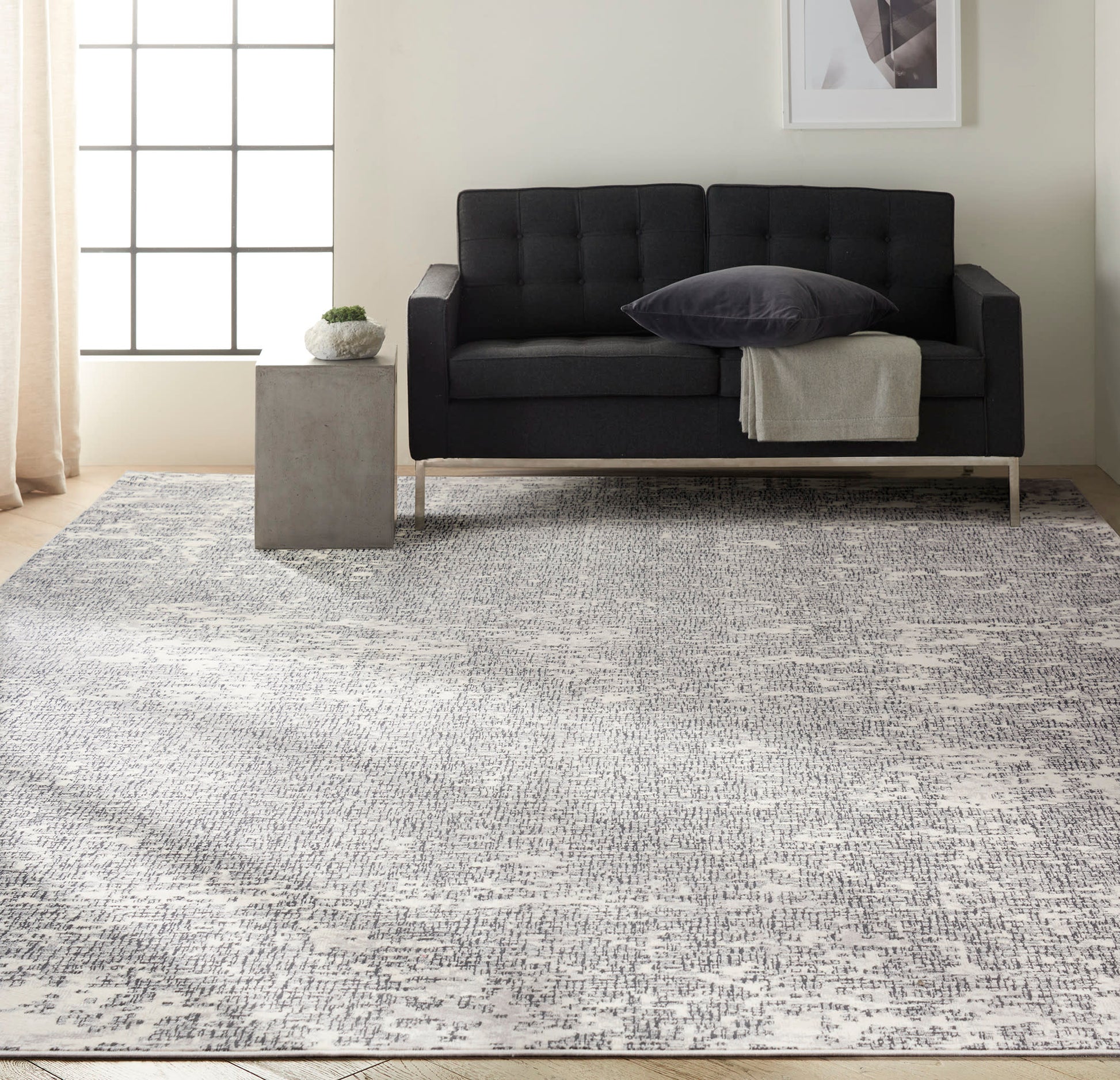 Charcoal tufted sofa on a gray patterned rug in a modern living room with a concrete side table, potted plant & beige curtains