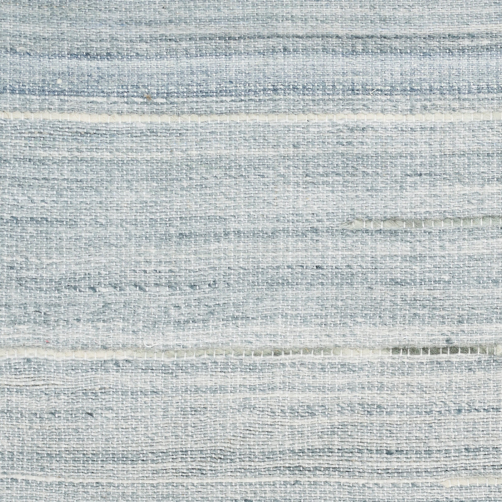 Light blue-gray woven rug with subtle horizontal stripes and a soft linen-like texture.