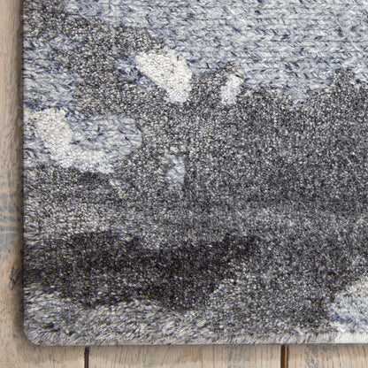 Blue-gray abstract patterned shag rug with thick plush pile, bound edges, laid on light wood floor.