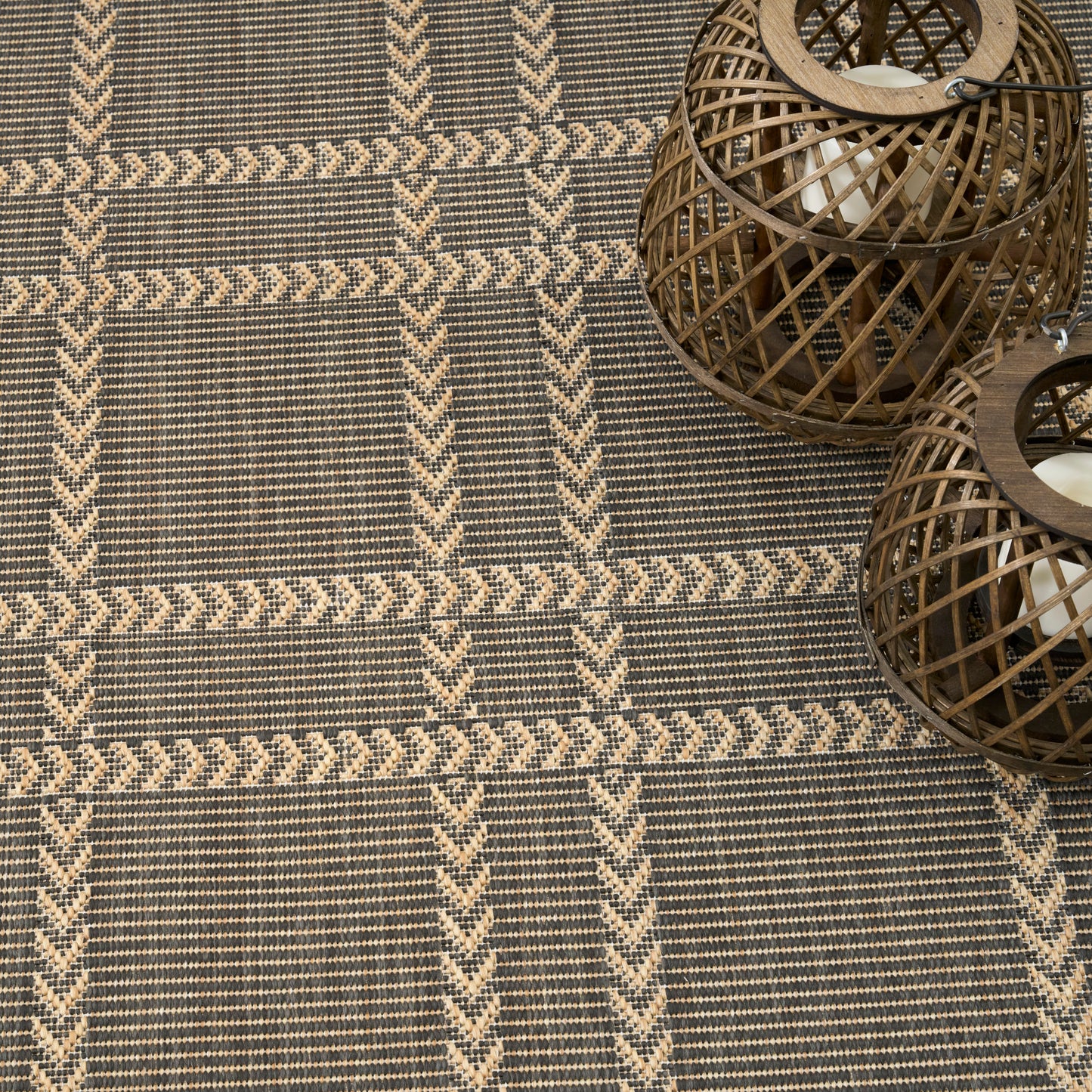 Natural woven rug with beige and taupe geometric stripes; two round wicker lanterns in the corner.