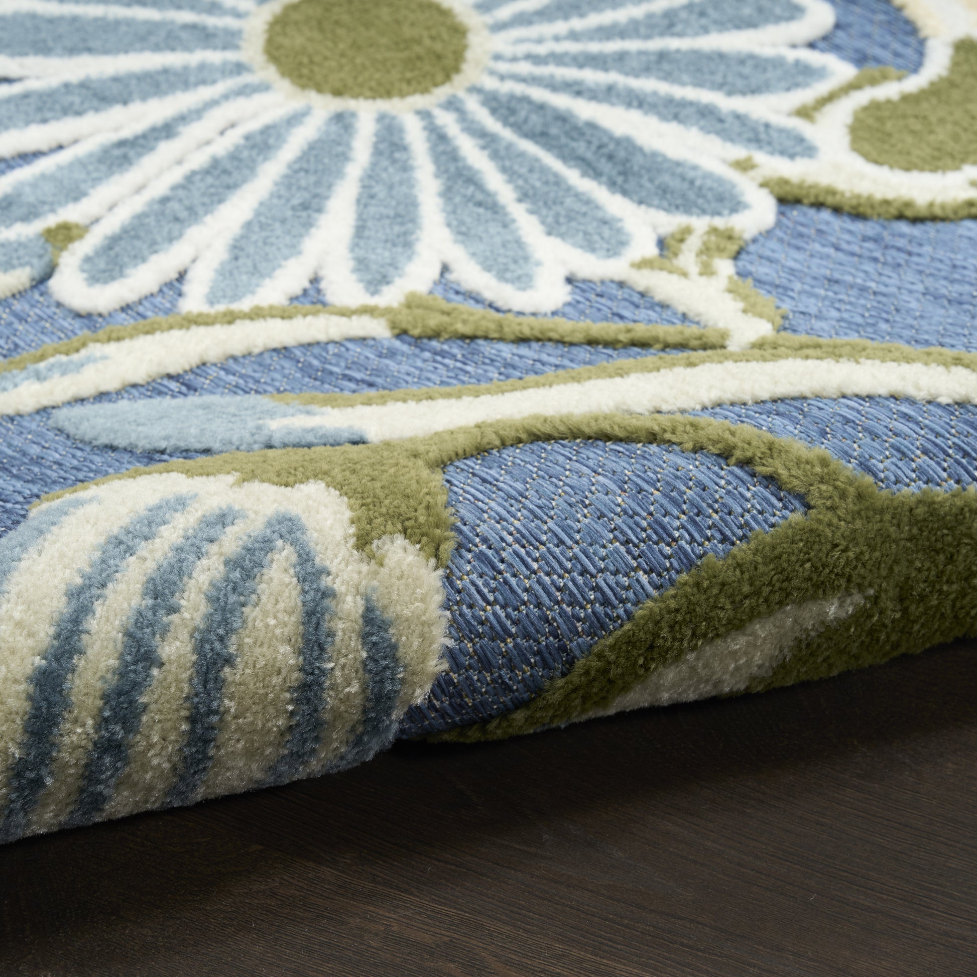 Close-up of blue floral rug with white petals and green stems on dark wood floor.