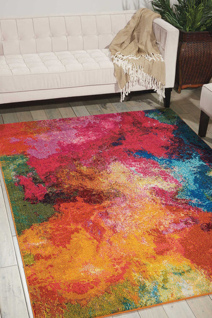 Vibrant abstract area rug with pink, red, orange, yellow, green and blue hues on a tiled floor beside a white tufted sofa.