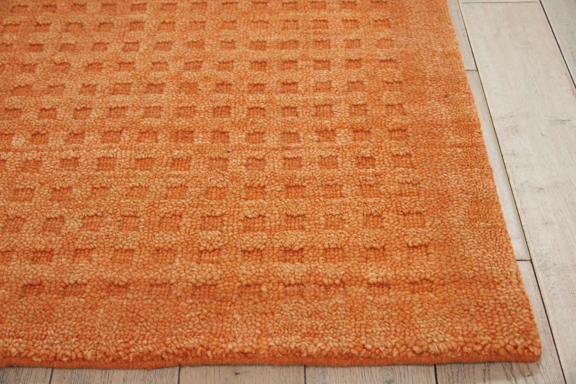 Orange textured shag rug with a subtle square pattern on light wood flooring.