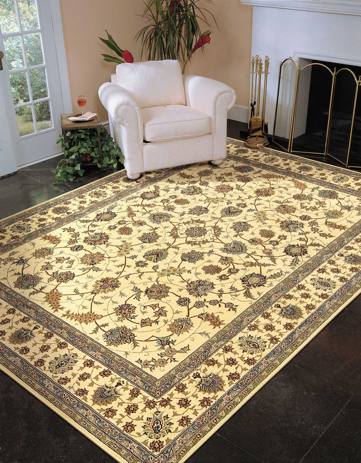 Cream armchair beside a large beige Persian-style floral area rug with gold borders in a living room near a fireplace.