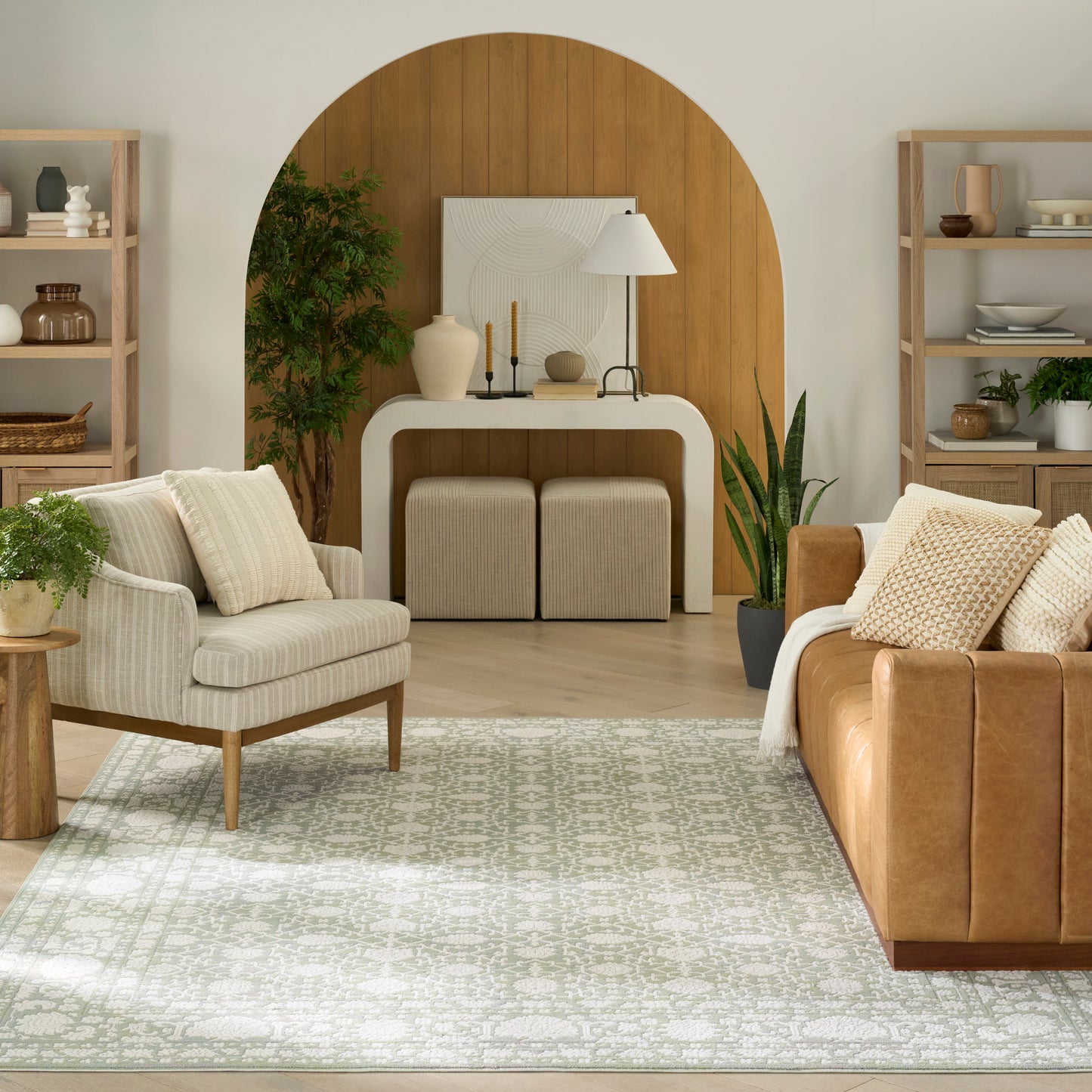 Neutral living room with an arched wooden backdrop, cream console, beige armchair, brown leather sofa, and a patterned rug.