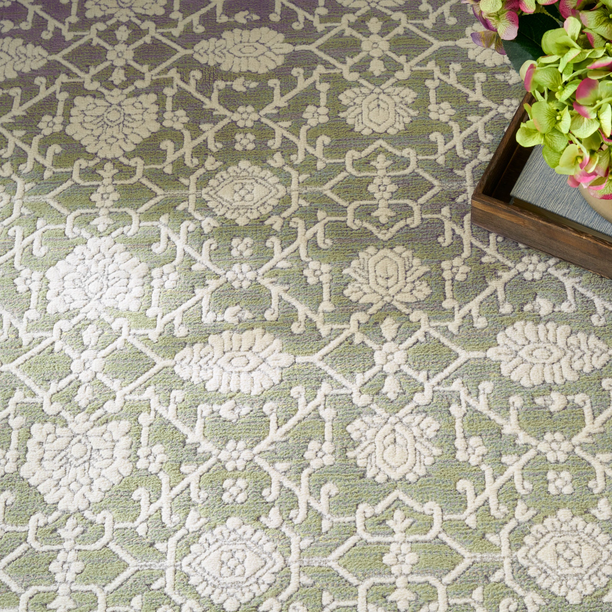 Green rug with cream raised floral lattice pattern; wooden tray corner with pink-green hydrangeas.