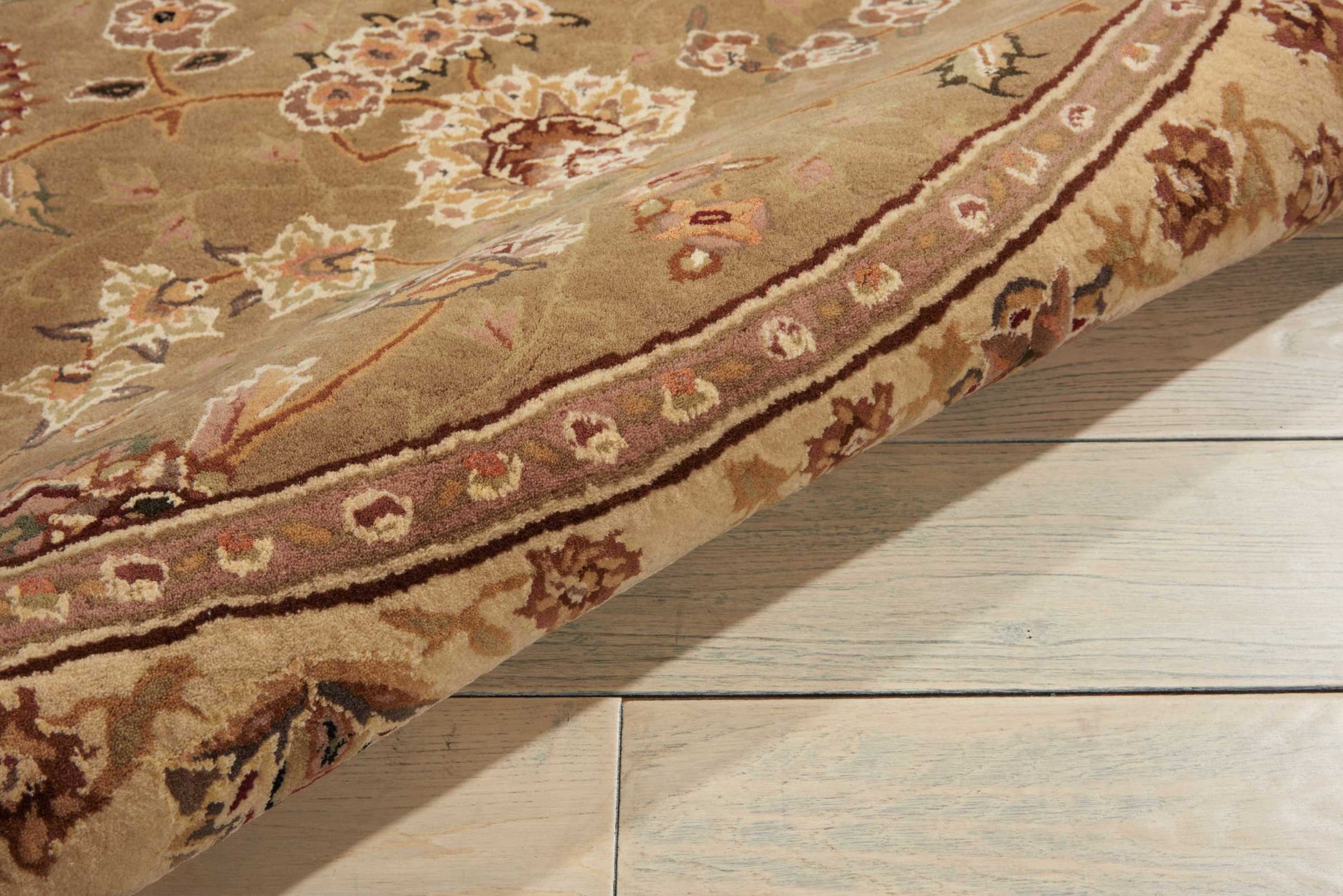 Beige Persian-style oriental rug with floral motifs and a bordered edge, folded on light wood flooring.