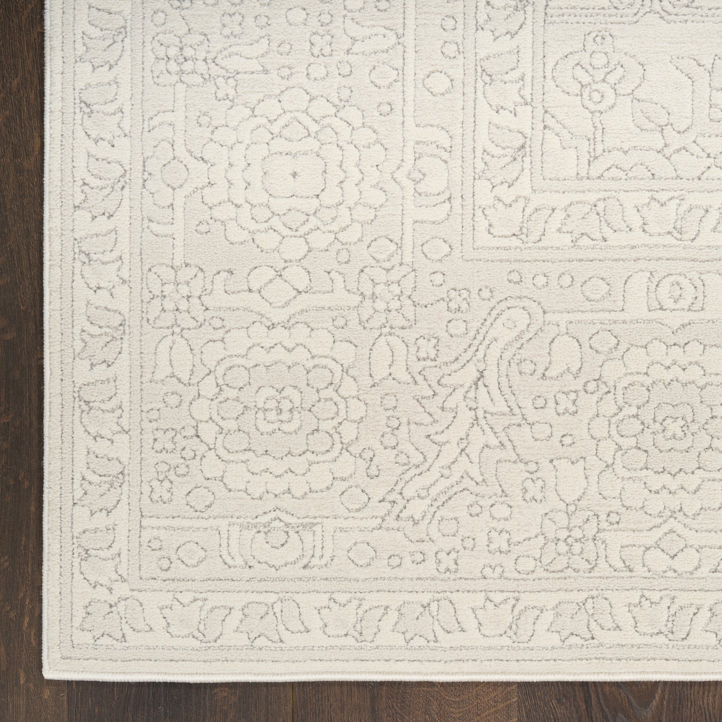 Cream ivory rug with ornate floral border and medallion-inspired central design on dark wood floor.