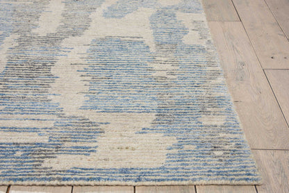 Blue and white abstract patterned area rug on light wood floor; soft, low-pile, modern geometric design.