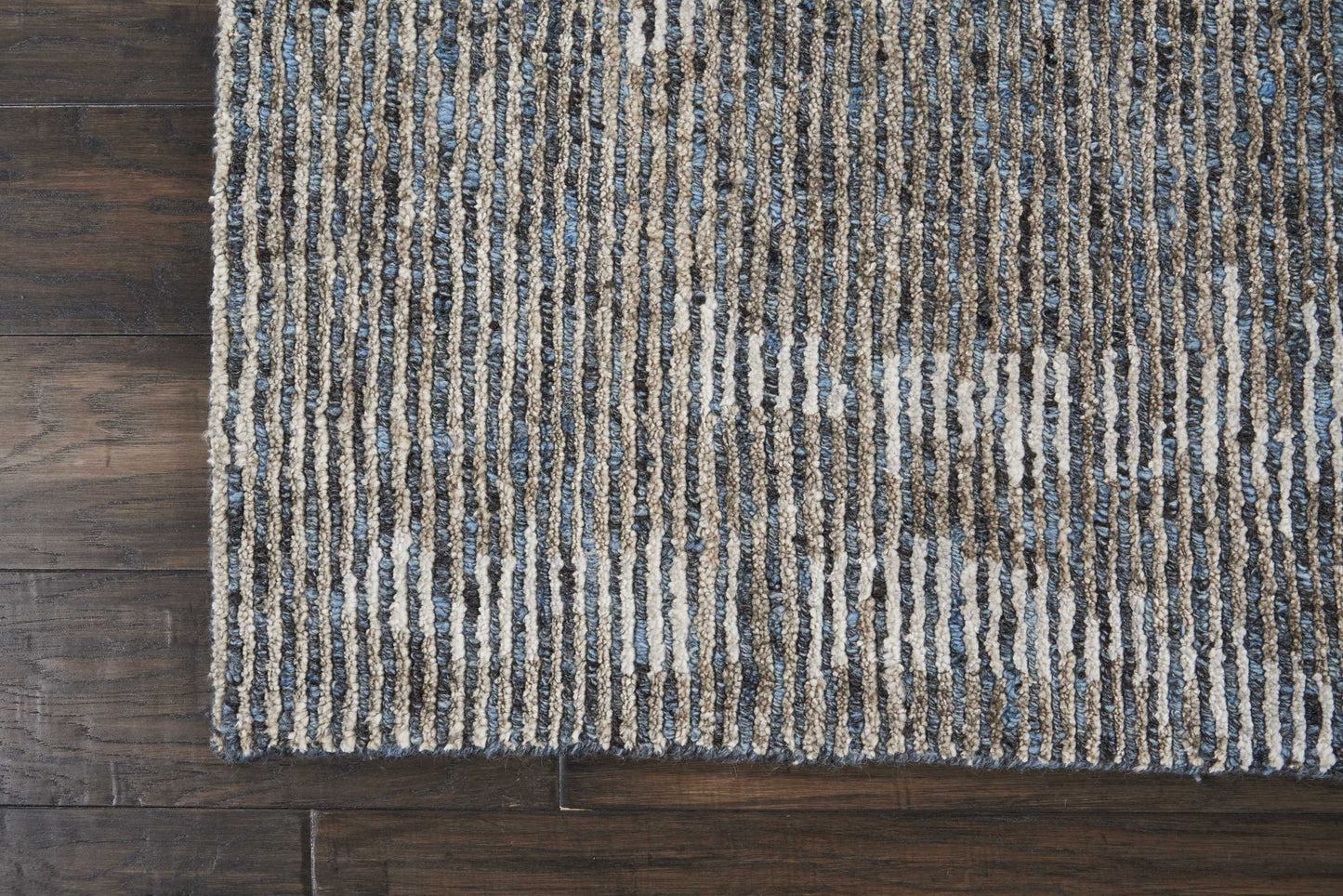 Rectangular shaggy loop-pile rug with blue, beige and gray vertical stripes on dark wood floor.