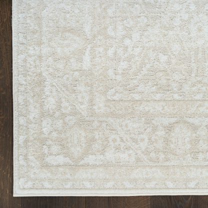 Beige area rug with subtle floral medallion pattern, light cream hues and white border on dark wood floor.