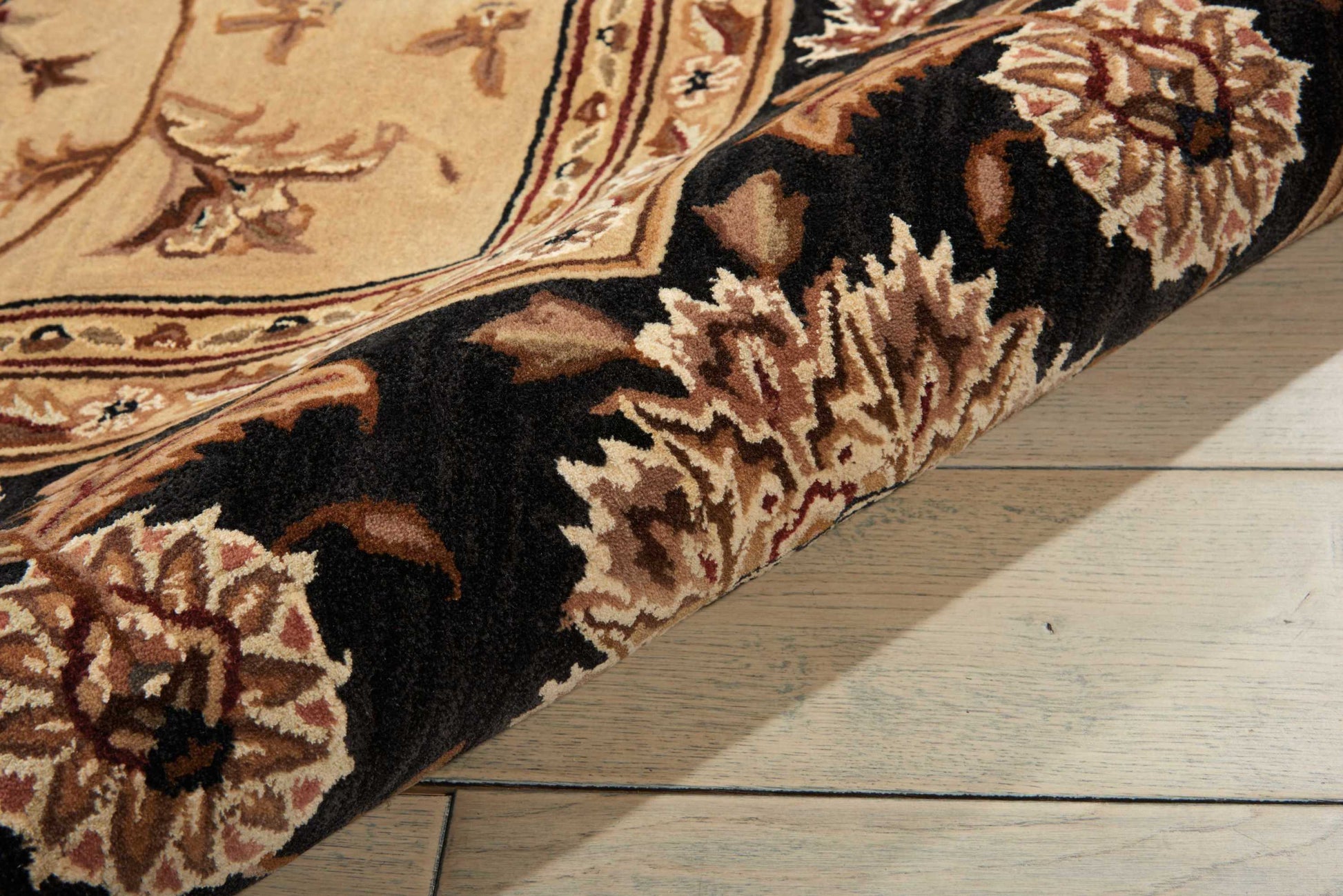 Rolled Oriental rug with beige field and ornate brown floral border on light wood flooring.