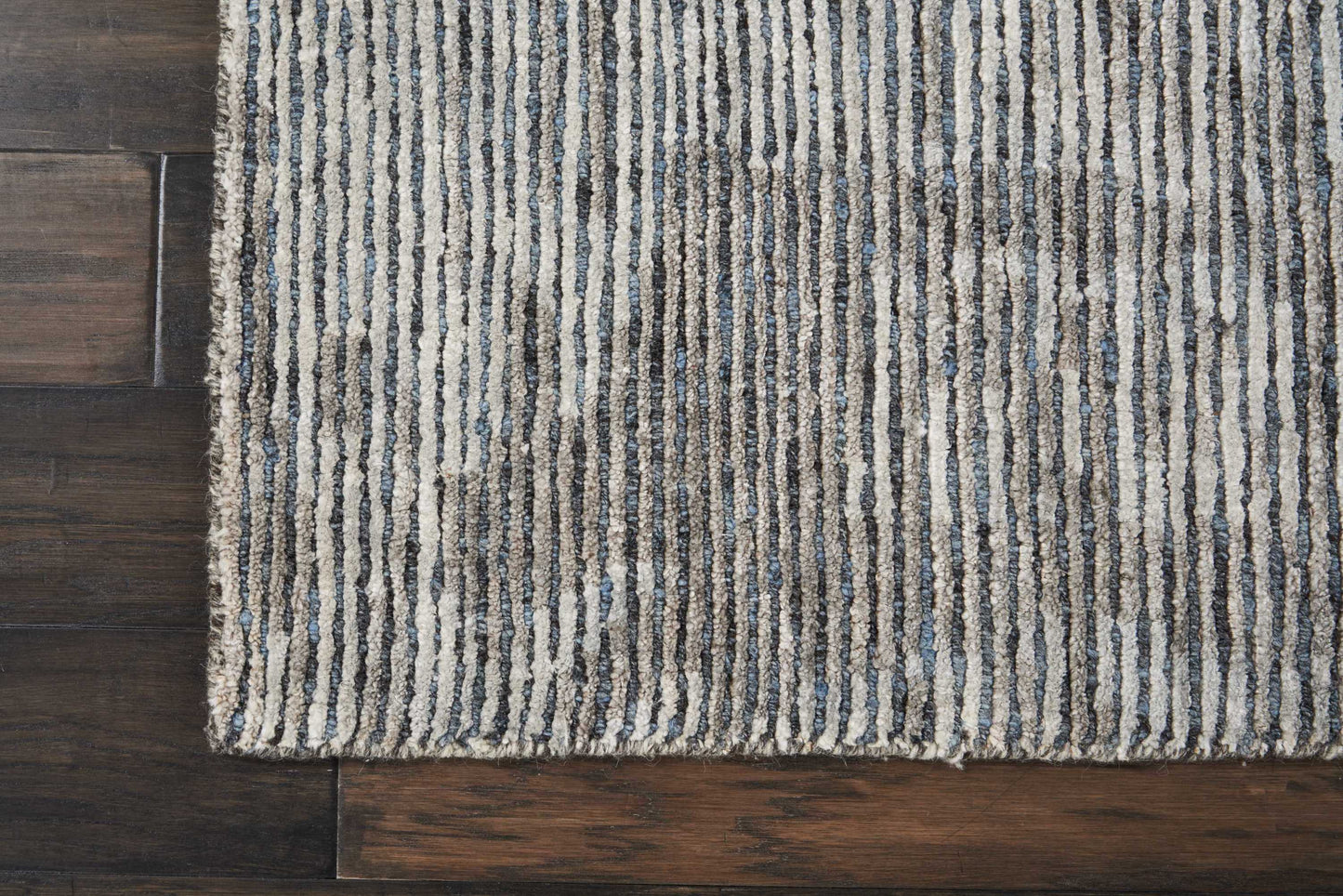 Light beige rug with dark blue vertical stripes on dark hardwood floor.