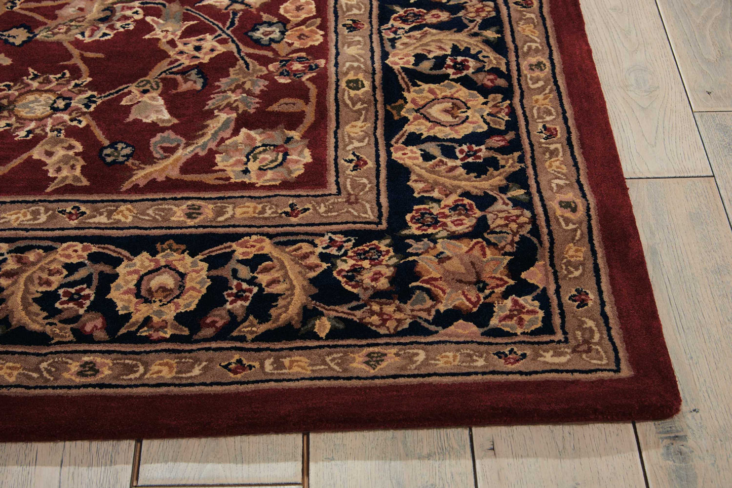 Decorative oriental rug corner with burgundy, navy and ivory floral border on light wooden floor.