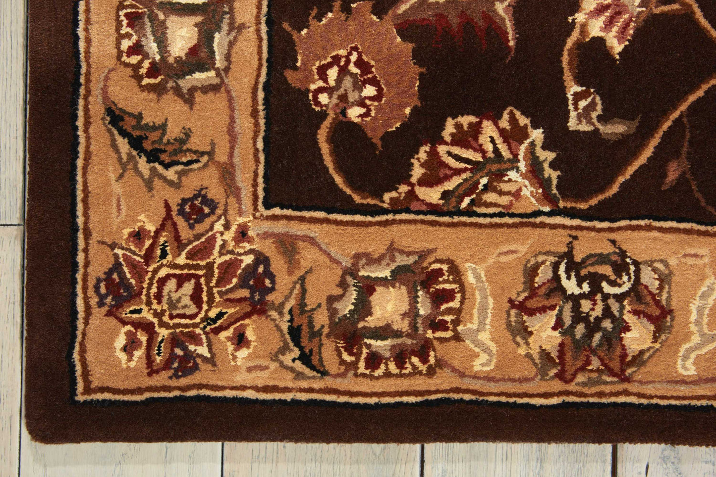 Traditional oriental rug corner with brown border, beige field and burgundy-cream floral motifs on wooden floor.