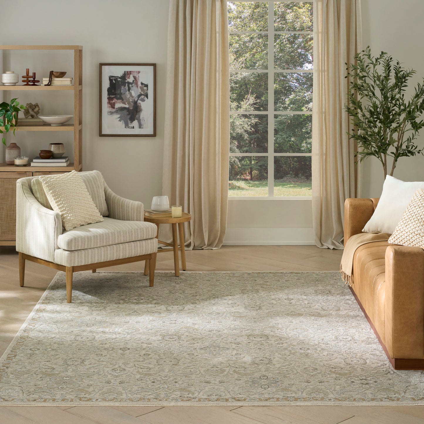 Bright living room with beige curtains, cream striped armchair, tan sofa, wooden shelf, abstract art, rug, plant by a window.