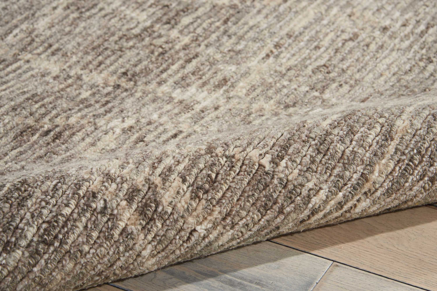 Beige-brown textured looped-pile rug, partially rolled, on light wooden floor.