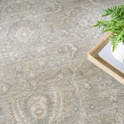 Light gray patterned area rug; wicker tray in corner holds a white pot with a green plant and a book.