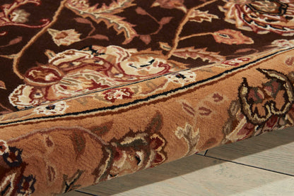 Close-up of a brown oriental rug with cream & red floral pattern & a rolled edge on a light wooden floor.