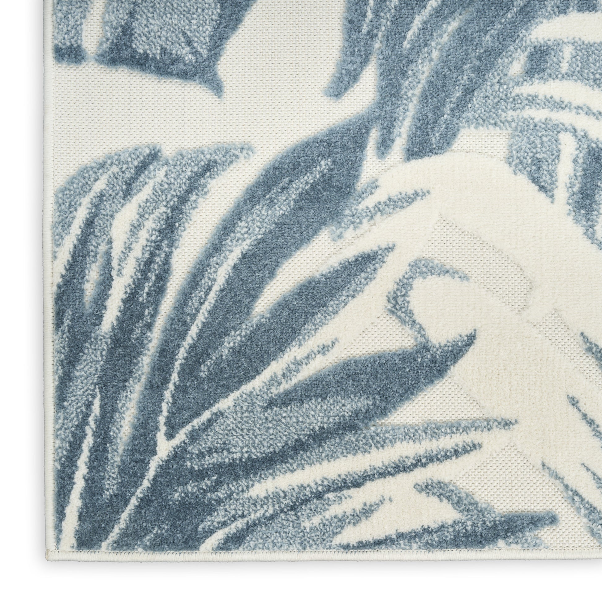 Blue palm-leaf pattern on a cream woven rug; textured tufted surface with visible edge stitching.