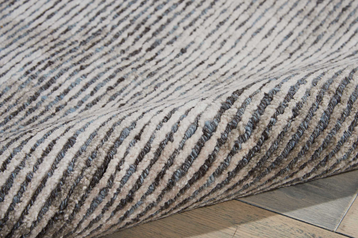 Textured beige and charcoal striped rug with thick pile, rolled edge on light wood floor.