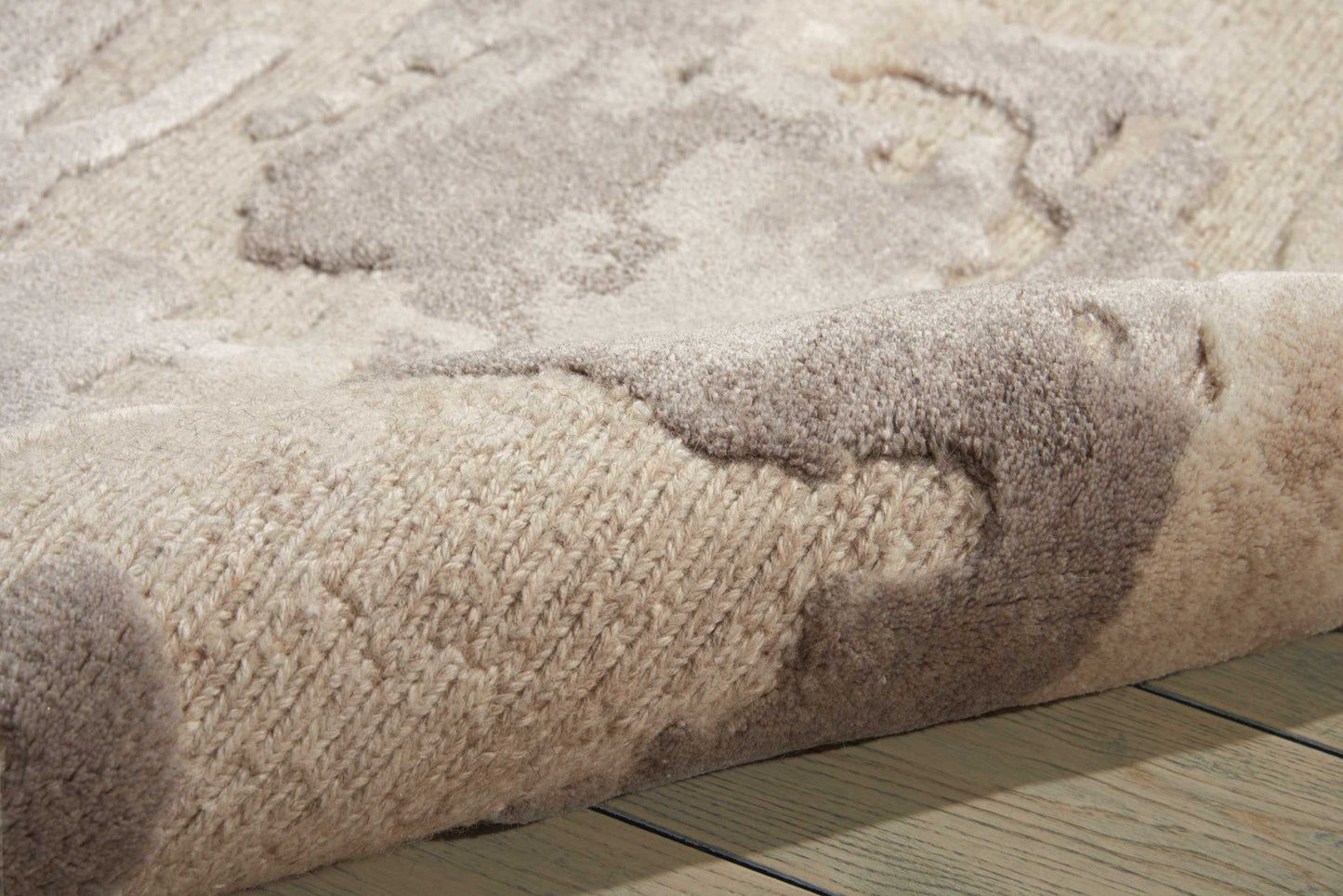Beige & taupe textured rug with plush high-pile, rolled edge on wooden floor.