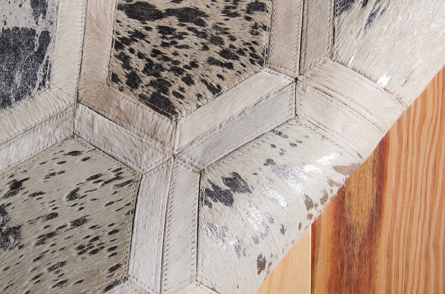 Hexagon patchwork cowhide upholstery in metallic gray-silver tones with stitched seams on leather furniture.