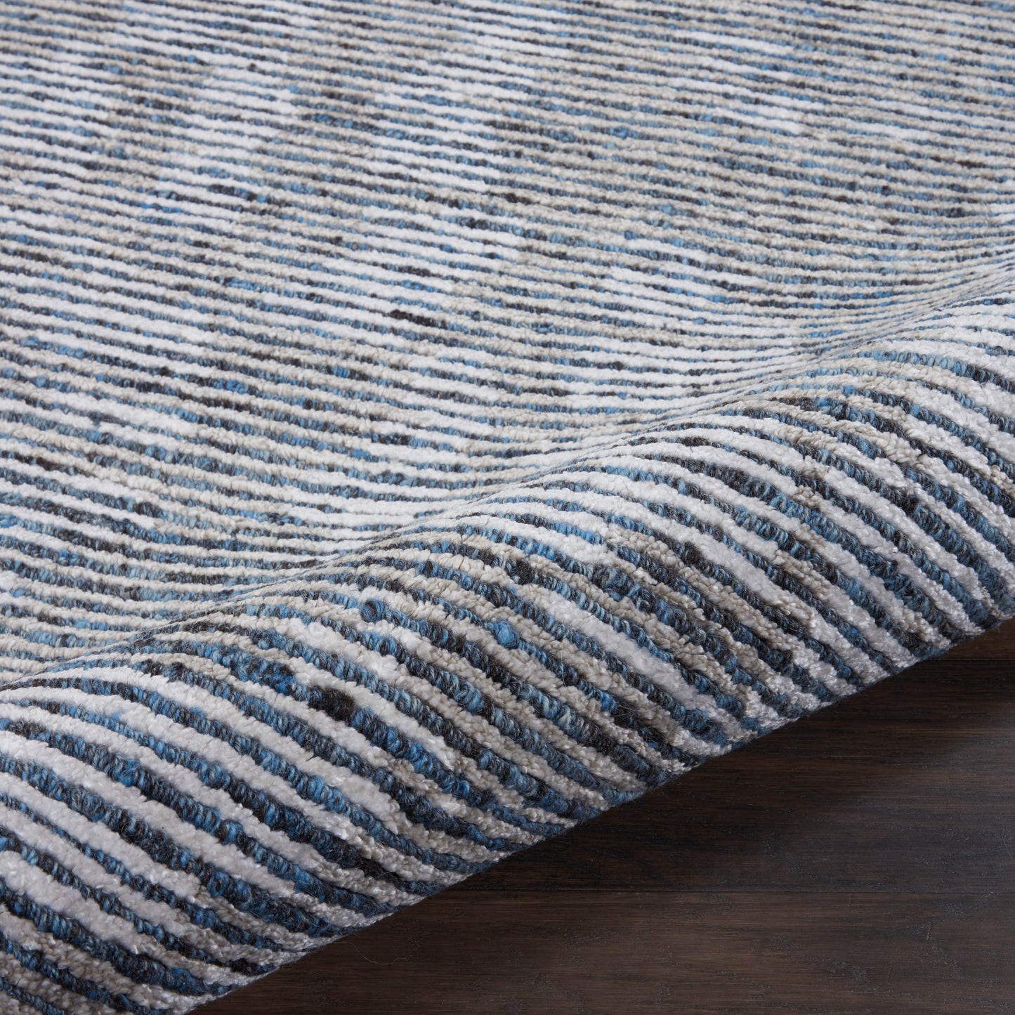 Blue and ivory striped textured rug with ribbed pile on dark wood floor.