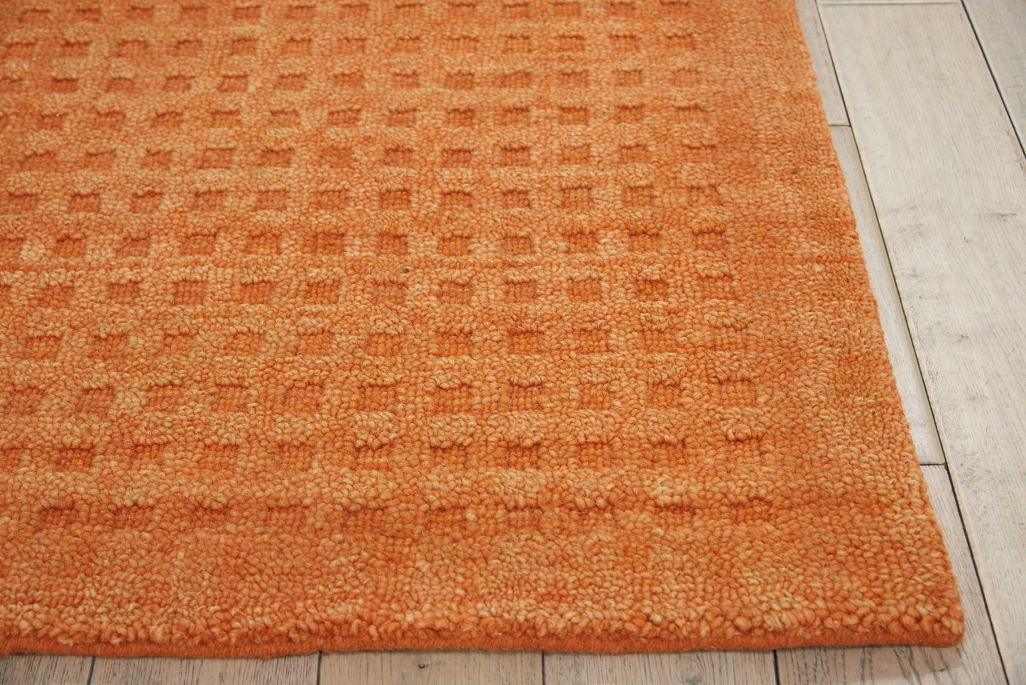 Orange textured area rug with a square-tufted pattern on light wood flooring.