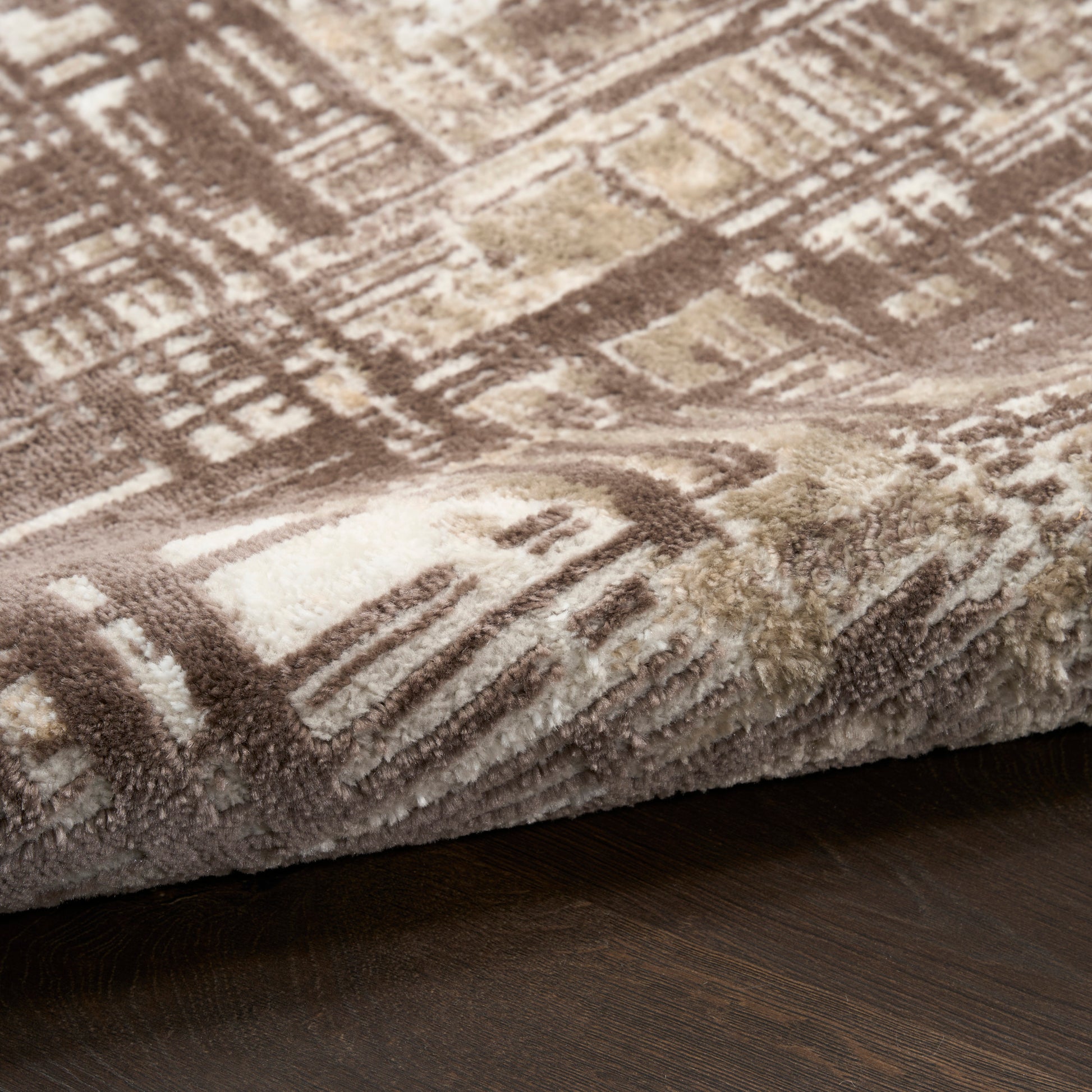 Plush geometric area rug in brown, tan & cream tones with shaggy pile on dark wood floor.