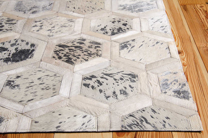 Geometric hexagon patchwork rug with cream and gray cowhide panels, beige trim, on wood floor.